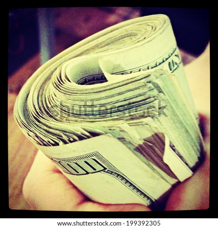 A hand holding a wad of cash with Instagram filter.