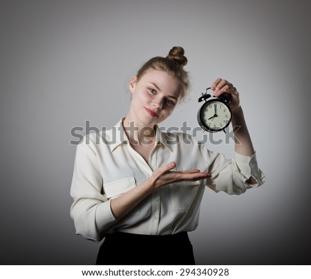 Young slim woman pointing at a clock on grey background. Eight o\'clock.