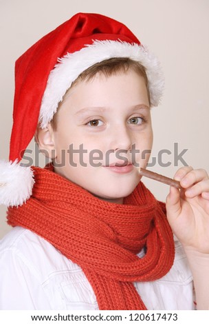 A cute boy in a red christmas hat and scarf  eating a chocolate