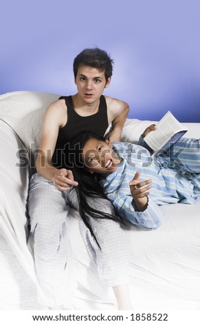 couple on couch pointing finger at camera over blue background