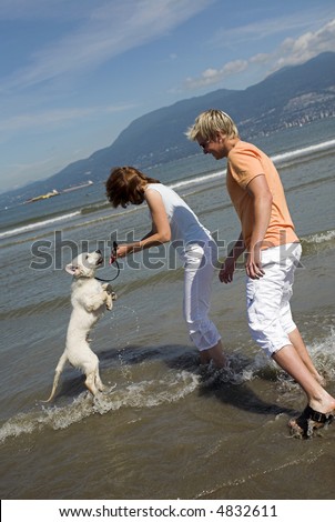 young couple playing with  dog on the beach vancouver