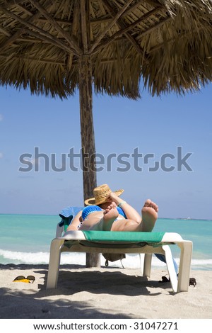 woman laying on deckchair under wood umbrella over blue sea and blue sky