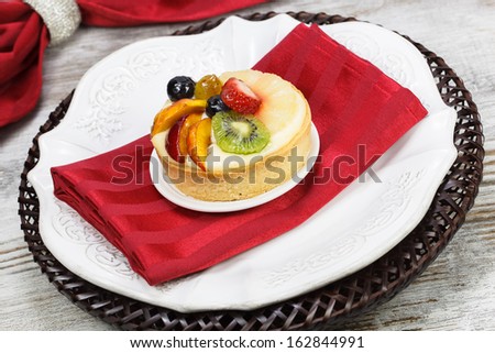 Fruit tart pies on white plate with forks , close up. A delicious fruit tart made with strawberries, peaches, grapes,  mango and kiwi.