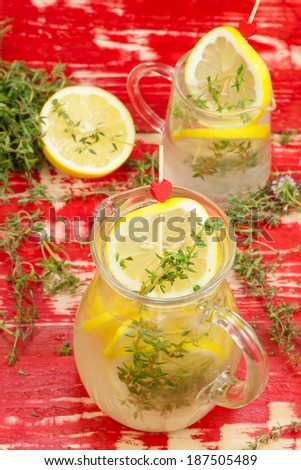 Lemon Thyme Lemonade. Summer Thyme Lemonade  in a glass jug and cup full of ice and lemon wedges and topped with thyme