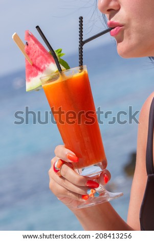 Fruit cocktail. Woman  with cocktail glass near sea. Blurred sea on background.