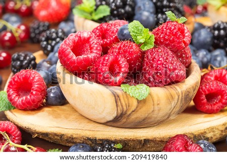 Fresh raspberries  in an olive wood bowl and  different fresh berries. Focus on raspberries. Macro, selective focus