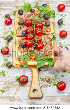 Pizza. Female hand holding a slice of homemade pizza with prosciutto, mozzarella and tomato with basil. Sicilian Style Square Pizza.