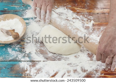 Woman pressing dough with rolling pin. Woman rolling dough with rolling pin on kitchen counter