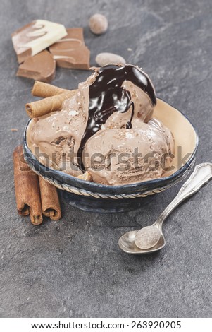 Ice cream with nuts and chocolate topping . Chocolate ice cream scoops with chocolate topping, nuts  and cinnamon on dark granite table. Macro photograph with shallow depth of field.