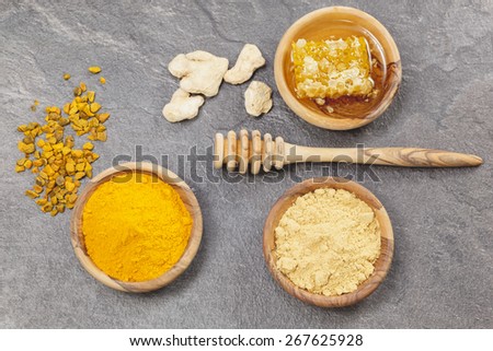 Ginger, Turmeric and honeycomb.  Ginger powder, root  and turmeric pieces, powder and honeycomb in olive wood bowls over dark granite table.  Macro photograph, selective focus