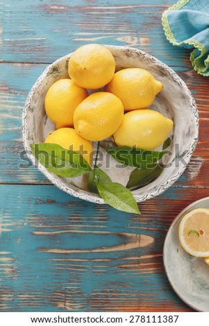 Lemons. Fresh lemons with leaves in rustic ceramic bowl over wooden background. Macro, selective focus, vintage style. Natural light