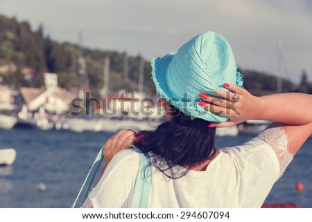 Woman with a hat looking at the sea during sunset.  Back view of a woman wearing a straw hat looking at the sea, near the yacht marine