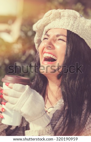Happy  woman with coffee cup, enjoying winter sun.  Beautiful woman in warm clothes holding coffee or tea,  looking up happy and smiling outdoors in a sunny winter day.vintage toning