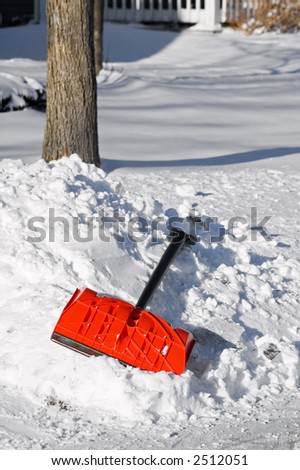 Orange snow shovel lies in snow pile next to shovel walk/driveway