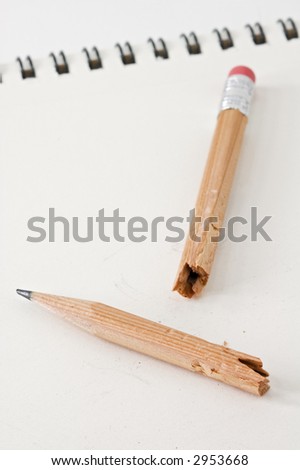 Broken and Chewed pencil lies on white pad - spiral binding out of focus in background