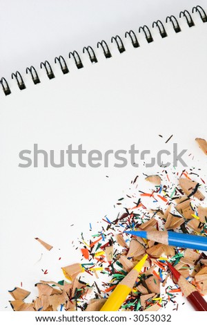 Yellow, red and blue color pencils and shavings lie on white spiral bound pad - white background