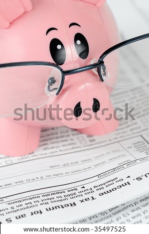 Piggy Bank Studies Tax Forms closeup - piggy bank in glasses pours over tax documents