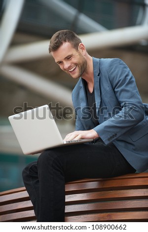 Portrait of a young businessman looking at laptop screen and smiling outdoors