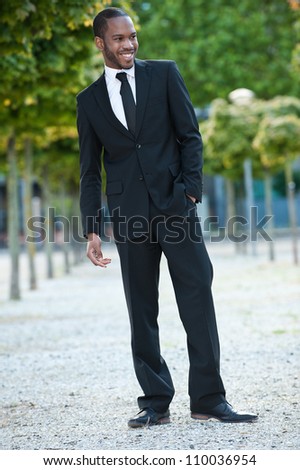 Smiling full body portrait of a young attractive African American business man wearing a suit outdoors.
