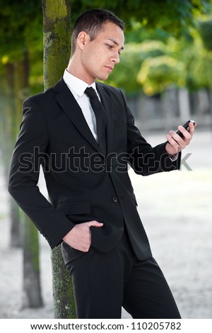 Portrait of a handsome young business man looking at message on his mobile phone outdoors.