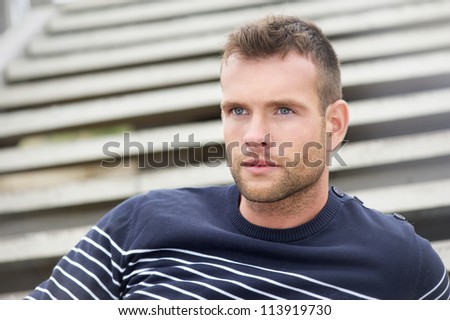 Portrait of a handsome young man sitting outdoors. Relaxed male model looking away with stairs in the background.
