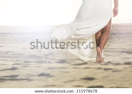 African American girl is walking on the sand with a flowing white dress.