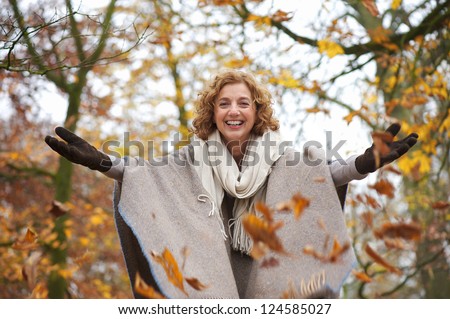 Middle aged woman throwing leaves in autumn with open arms