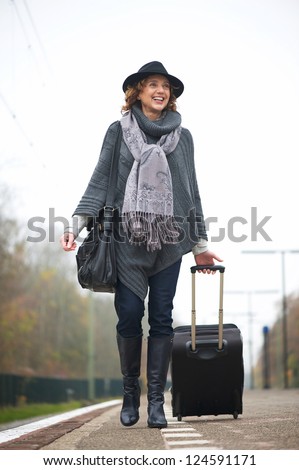 Smiling woman walking on train station platform with travel bag