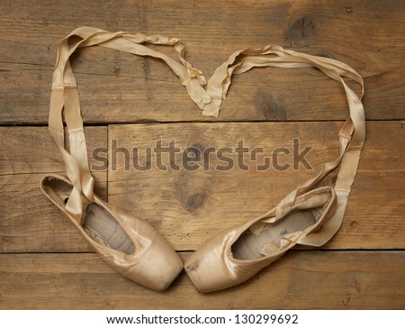 Pair of ballet shoes on wooden floor with ribbon in heart shape - above view