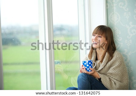 Portrait of a young woman sitting by window with cup of tea