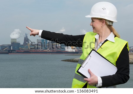 Portrait of a female inspector in hardhat and safety vest pointing finger at industrial site