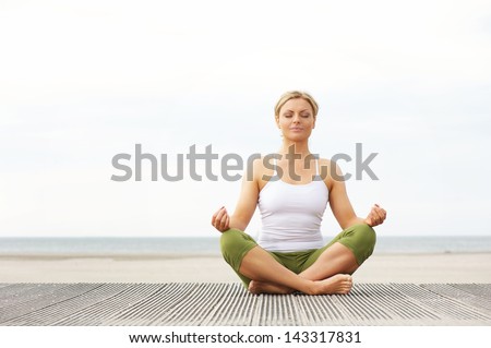 Portrait of a beautiful young woman sitting in yoga pose at the beach