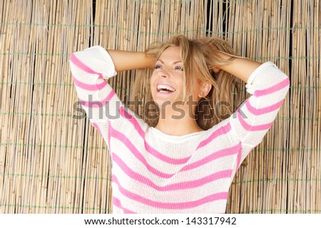 Close up portrait of a beautiful blond woman standing outdoors laughing with hands in hair