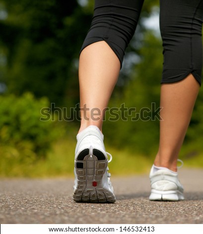 Young woman in white sneakers walking outdoors from behind
