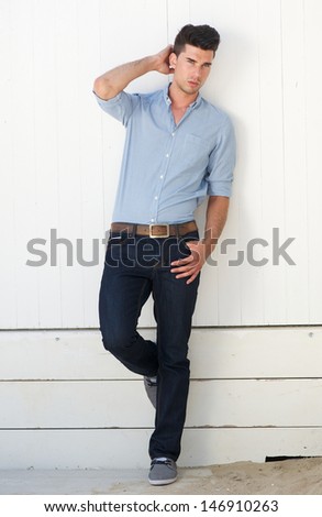 Full length portrait of a handsome male fashion model standing against white wall outdoors