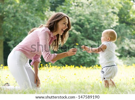 Portrait of a happy mother teaching baby to walk in the park