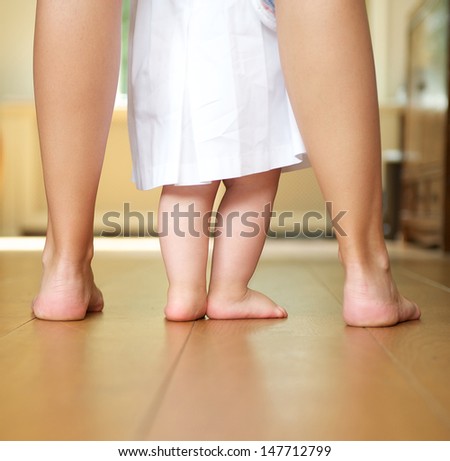 Closeup Portrait Of A Mother Helping Baby To Walk Indoors