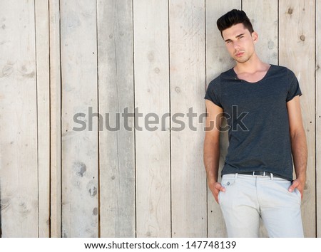 Portrait of a cool young guy posing outside against wooden wall