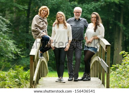 Portrait of a happy family with mother father and daughters standing on bridge in the forest