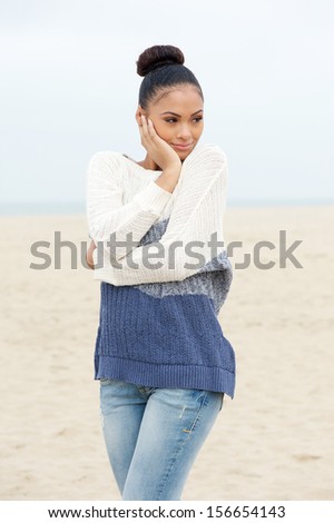 Portrait of a pretty young woman standing on beach alone in sweater and jeans