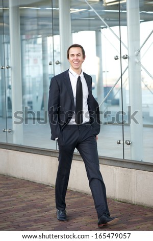 Full body portrait of a happy businessman in suit walking on sidewalk in the city