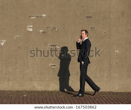 Full body portrait of a young businessman walking and talking on mobile phone