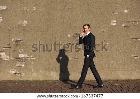 Full body portrait of a smiling businessman walking and talking on mobile phone