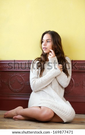 Portrait of a beautiful young woman in sweater sitting on wood floor at home