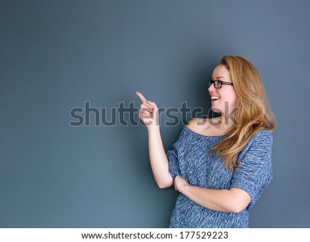 Close up portrait of a smiling woman pointing finger up against gray background