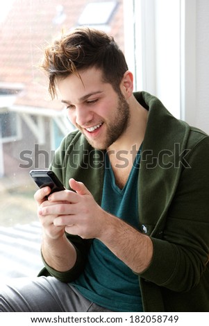 Close up portrait of a young man smiling and looking at message on mobile phone