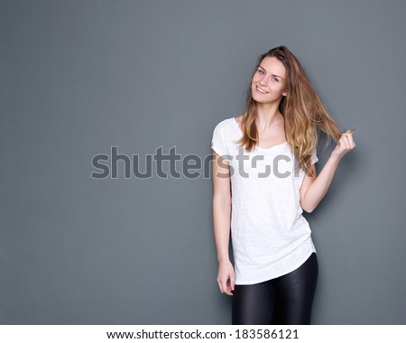 Portrait of a cute young woman smiling with hand in hair on gray background