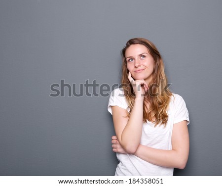 Close up portrait of a young woman thinking with hand on chin on gray background