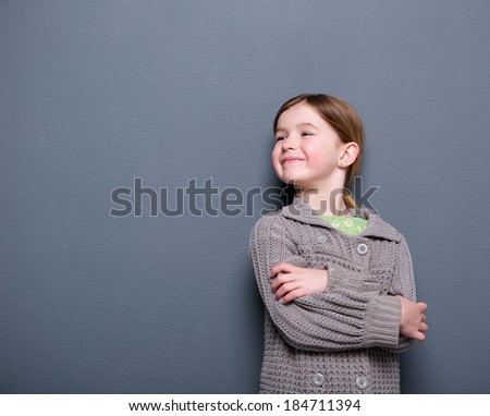 Close up portrait of an cute child of elementary age smiling with arms crossed on gray background