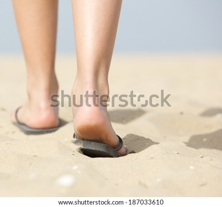 Close up from behind rear view woman walking in slippers on sand at beach